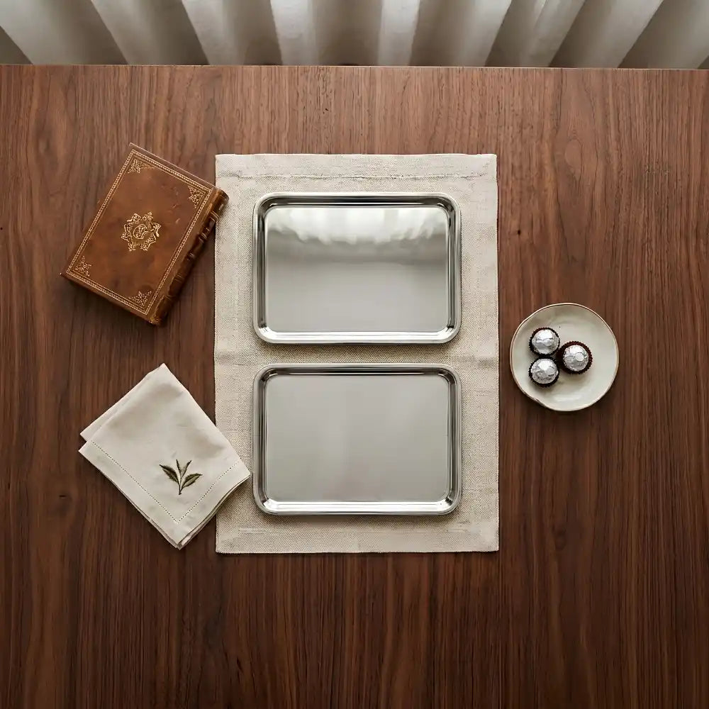 Two silver trays on a wooden surface with a book and small dish.