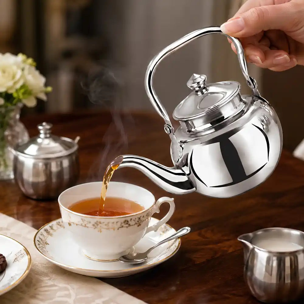 Silver teapot pouring tea into a white cup on a wooden table with a blurred background