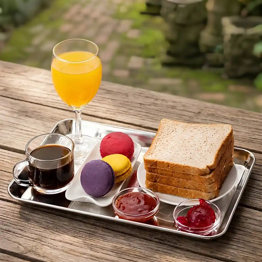 Tray with a glass of orange juice, cup of coffee, toast, and colorful macarons on a wooden surface.